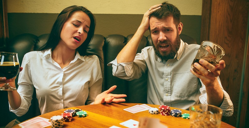 Man and woman playing card game with alcohol in their hands